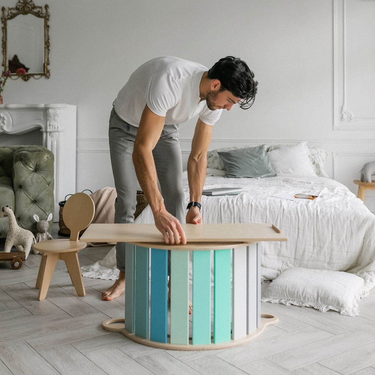 Mint-colored set including a seesaw, double-sided board, and mini chair with a man leaning over a bed, in a cozy room setting.