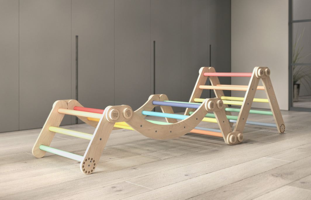 Children&#39;s rainbow-colored climbing set with two Pikler triangles and a swing, made from birch wood.