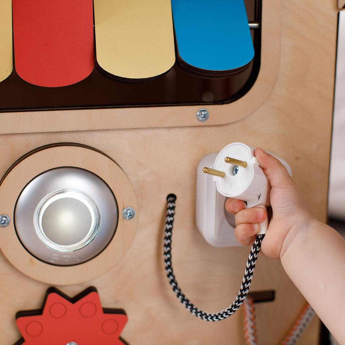 Wooden busy board with colorful sliders and child holding a plug.