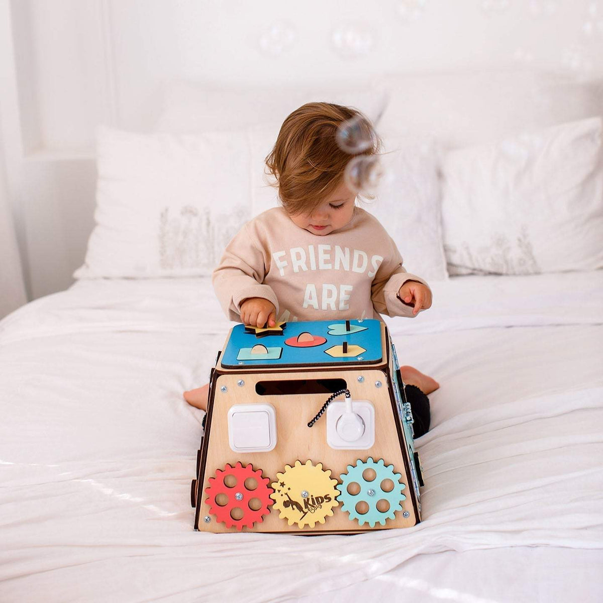 Child playing with Montessori wooden activity board on bed.