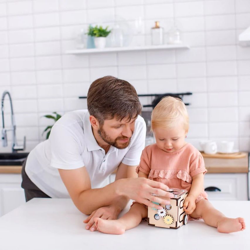 Father and child playing with wooden activity cube in kitchen setting.