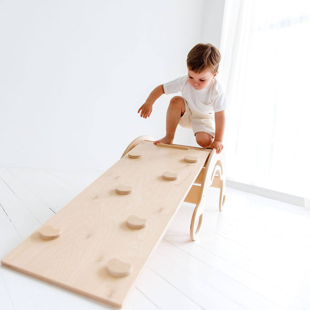 Child climbing Montessori 5-in-1 wooden rocker with birch plywood board.