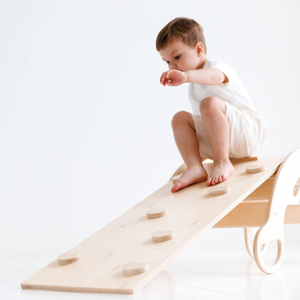 Child playing on natural wood Montessori rocker with climbing board, enhancing motor skills.