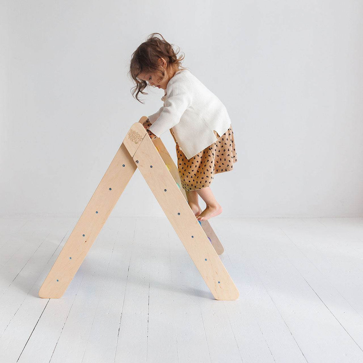 Child climbing on &quot;Kletterdreieck – Hell&quot; wooden climbing structure in light color.
