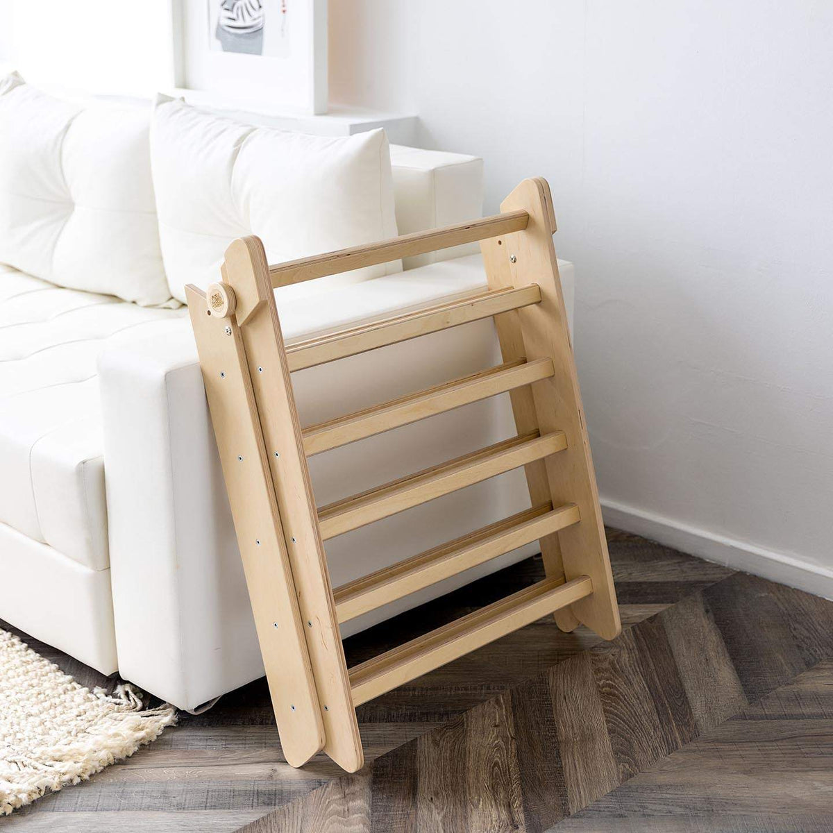 Natural wooden climbing triangle with slide/ladder for children, shown folded in a living room setting.