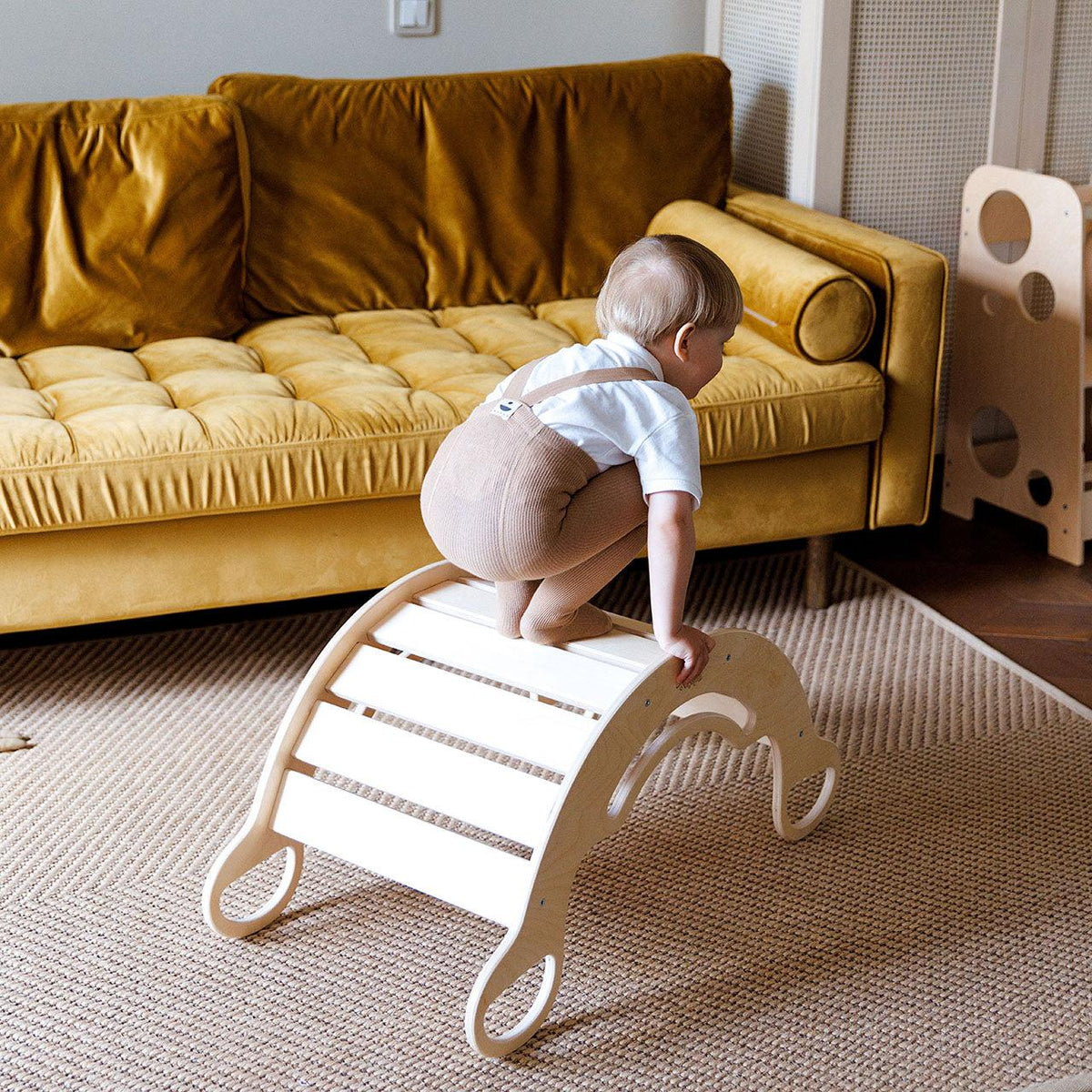 Child climbing on Montessori wooden rocker with reversible board, promoting motor skills development.