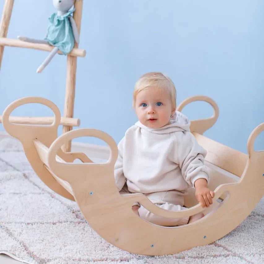 Toddler playing on a natural wood balance rocker in a cozy room setting.
