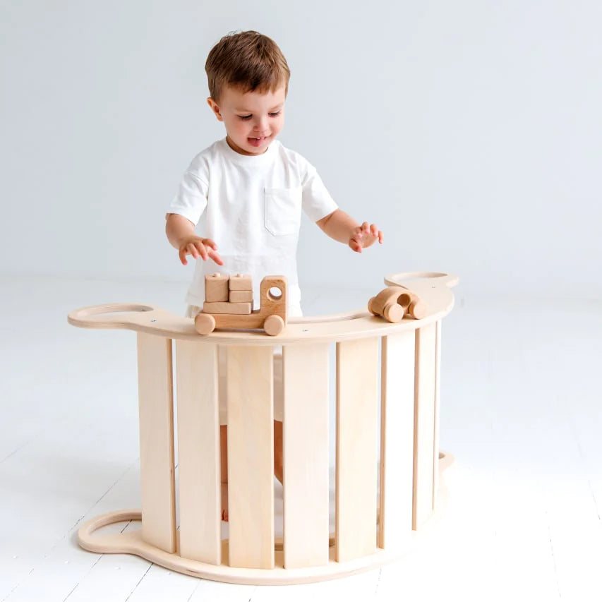 Toddler playing with wooden balance rocker in natural finish, promoting movement and creativity.