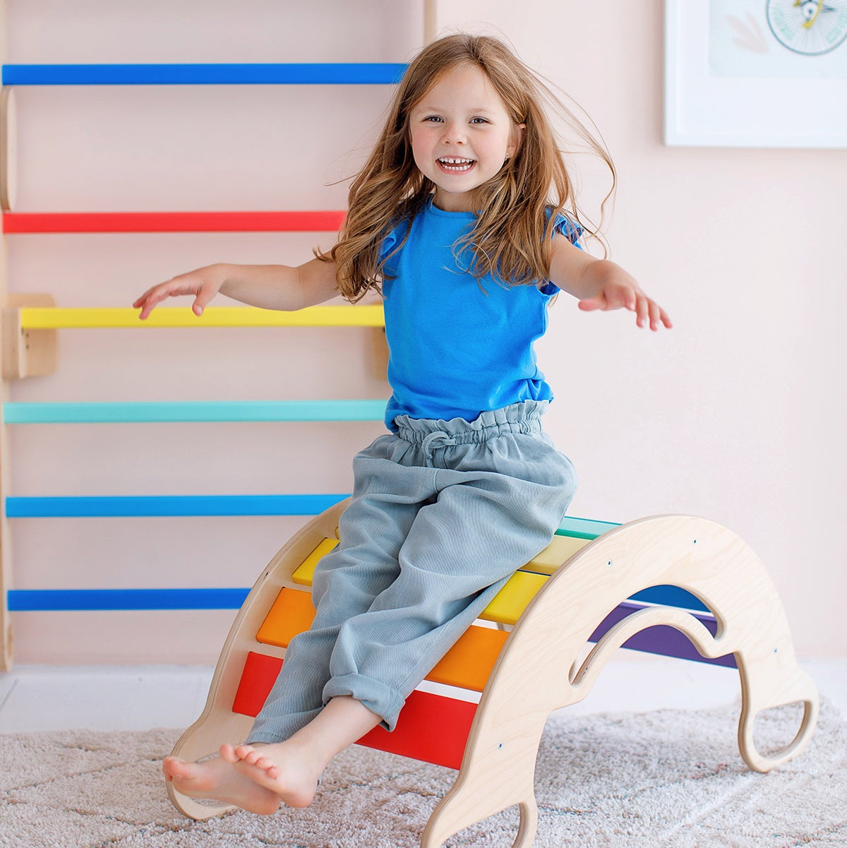 Child playing on a colorful wooden rocker in a bright room.
