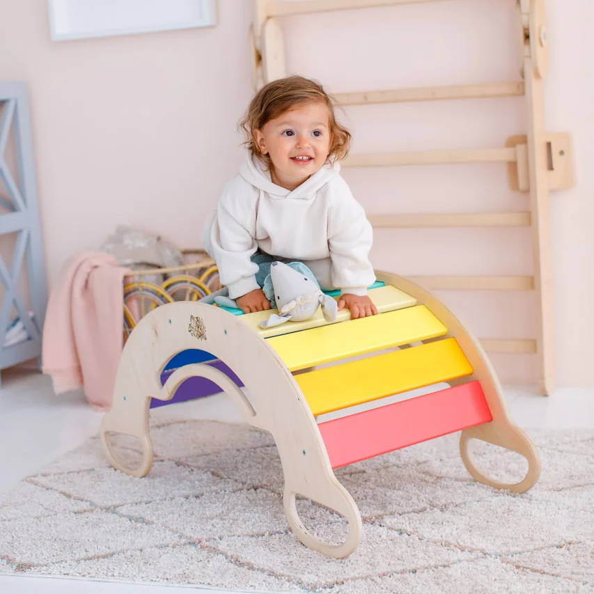 Multifunctional wooden rocker for toddlers in bright colors, serves as swing, climbing frame, and seating, ideal for motor skill development.
