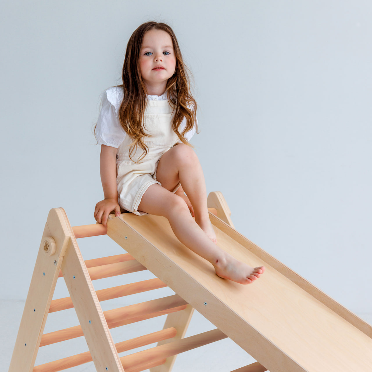 Child on uncoated wooden Pikler triangle and slide from large play set.