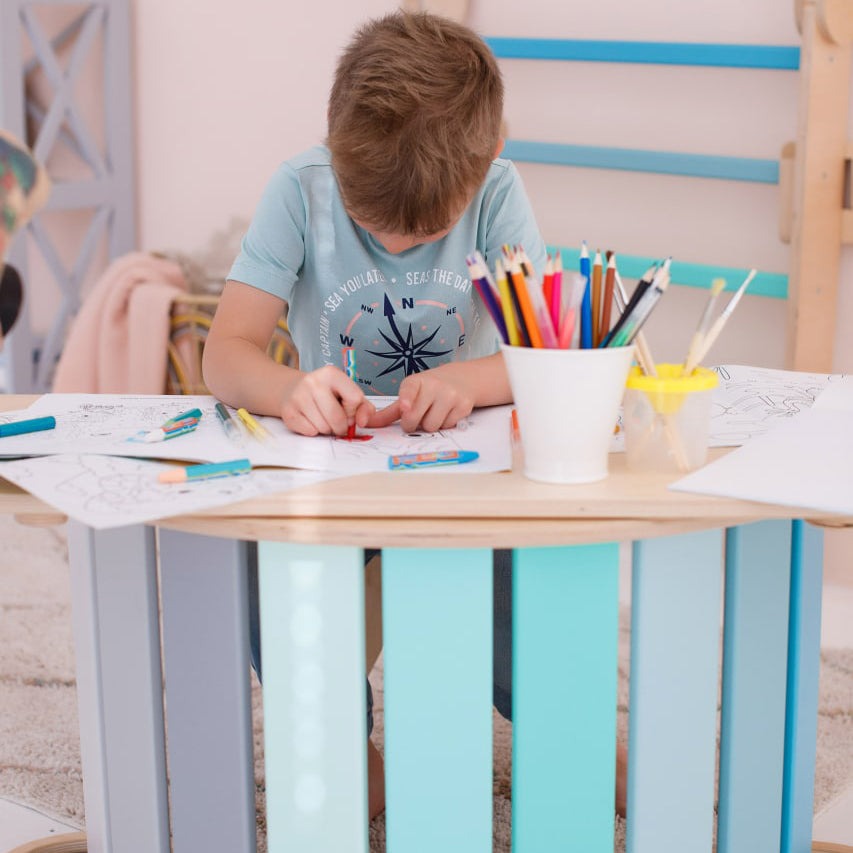 Child playing with a mint green set including a seesaw, double-sided board, and mini chair.