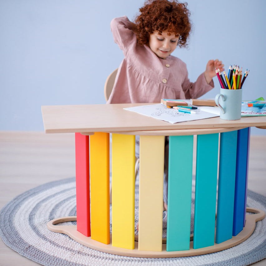 Child using colorful set of seesaw, double-sided board, and mini chair in bright room.