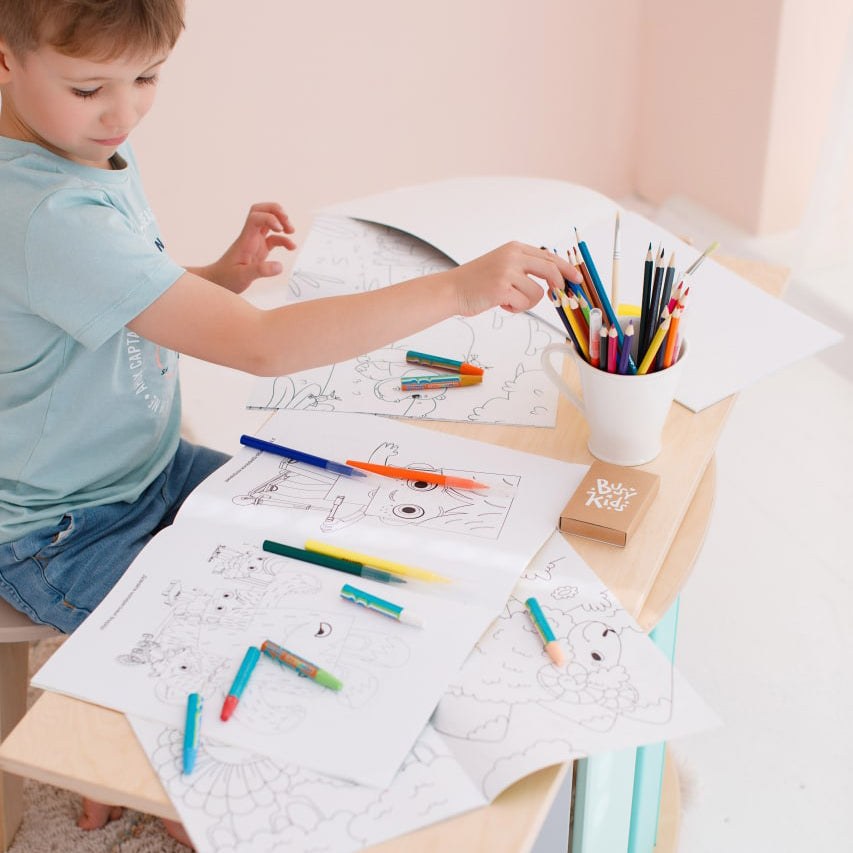 Child using mint-colored mini chair and table set with coloring sheets and pencils.