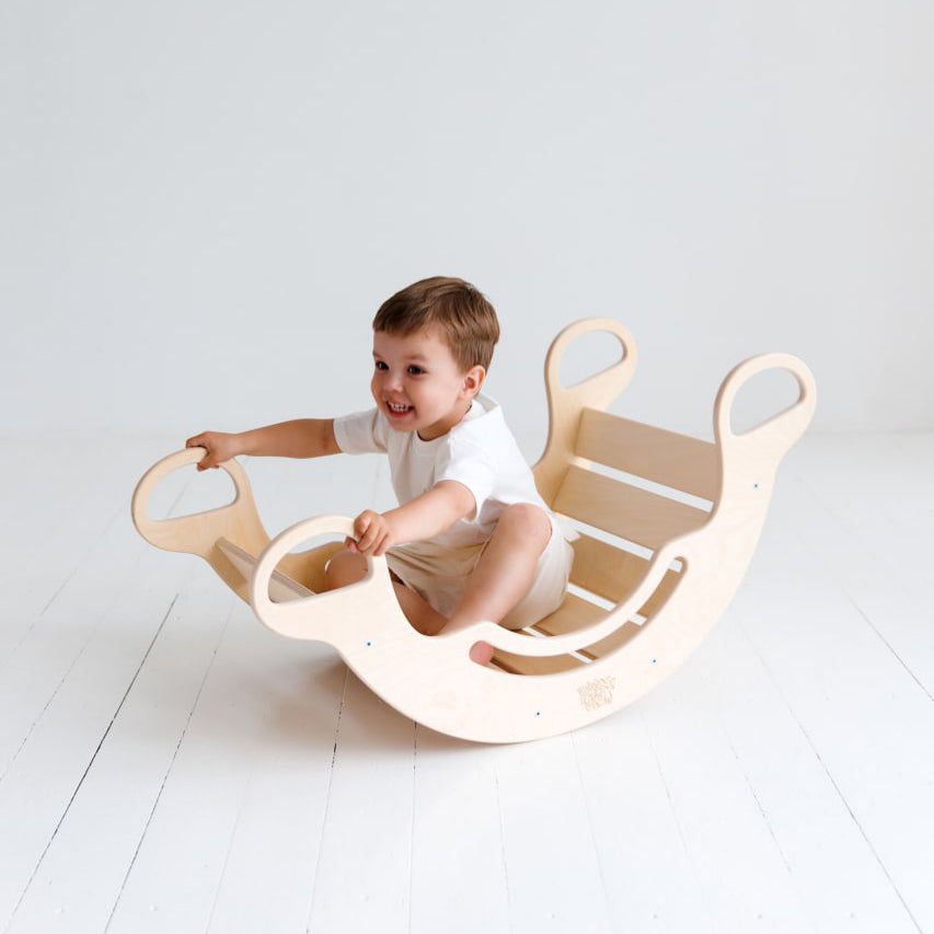 Child playing with a natural wooden balance rocker featuring a double-sided board for motor skill development.