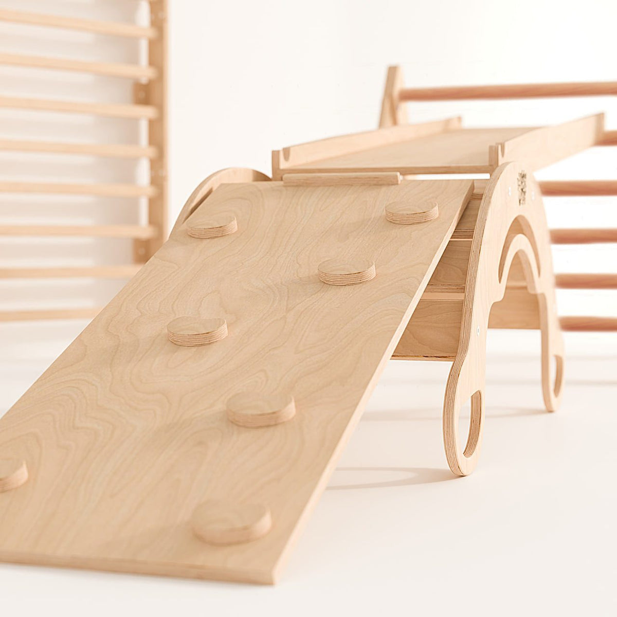 Eco-friendly wooden play set with Pikler triangle, two slides, and balance rocker, uncoated finish.