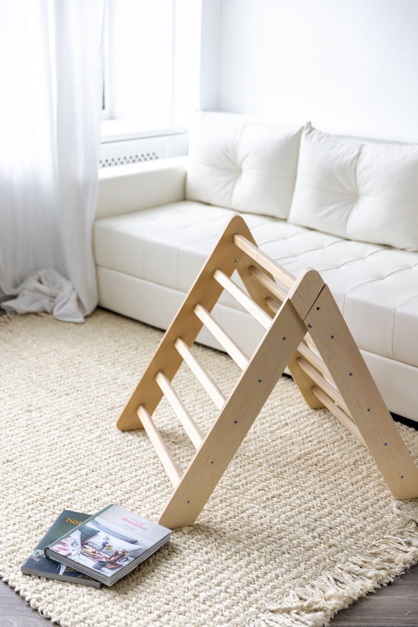 Play set with climbing triangle and dual-sided board in natural wood, set on a beige carpet in a cozy living room.