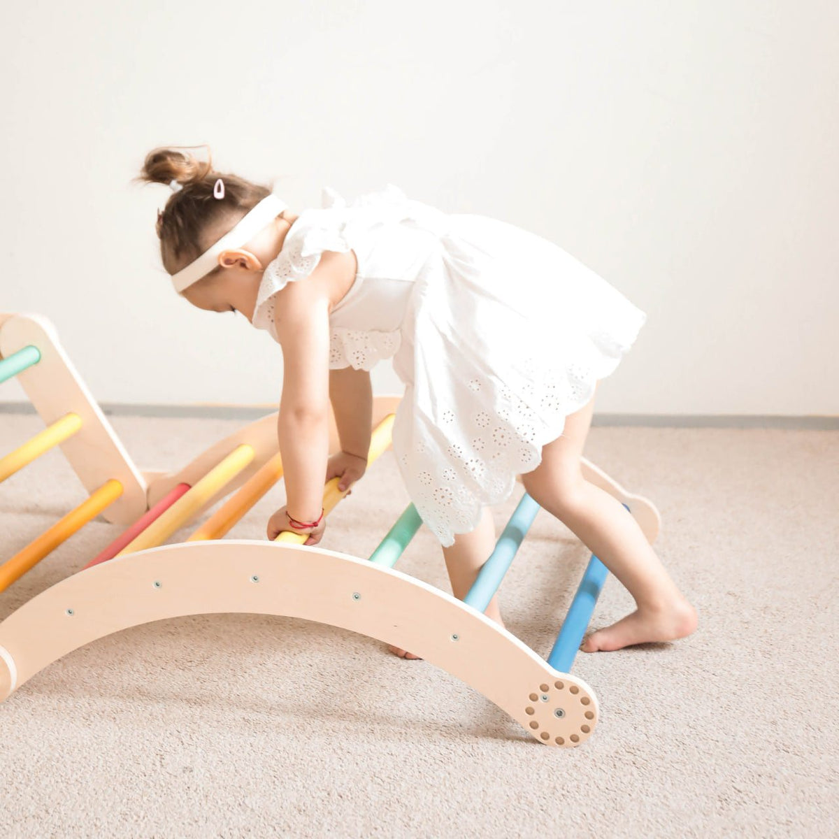 Child playing on rainbow-colored wooden climbing set for kids.