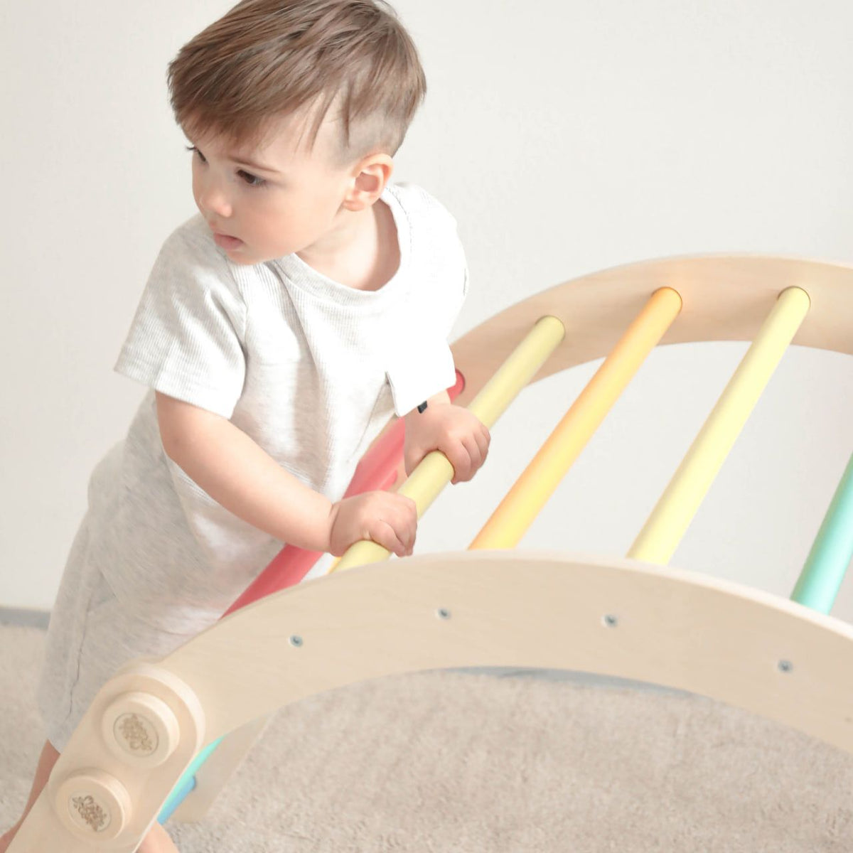 Child playing on a rainbow-colored wooden climbing frame set.