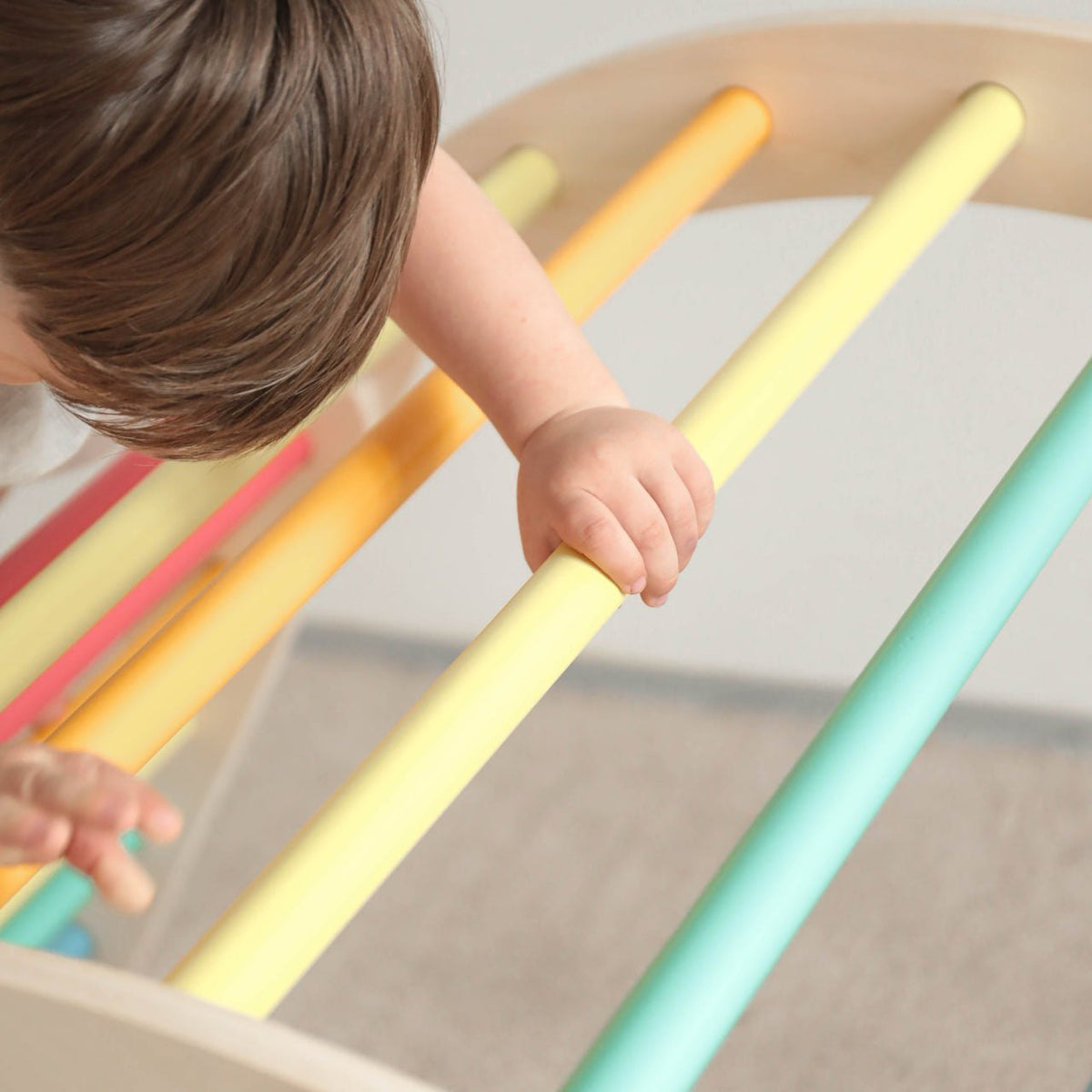 Child climbing on rainbow-colored wooden playset bars