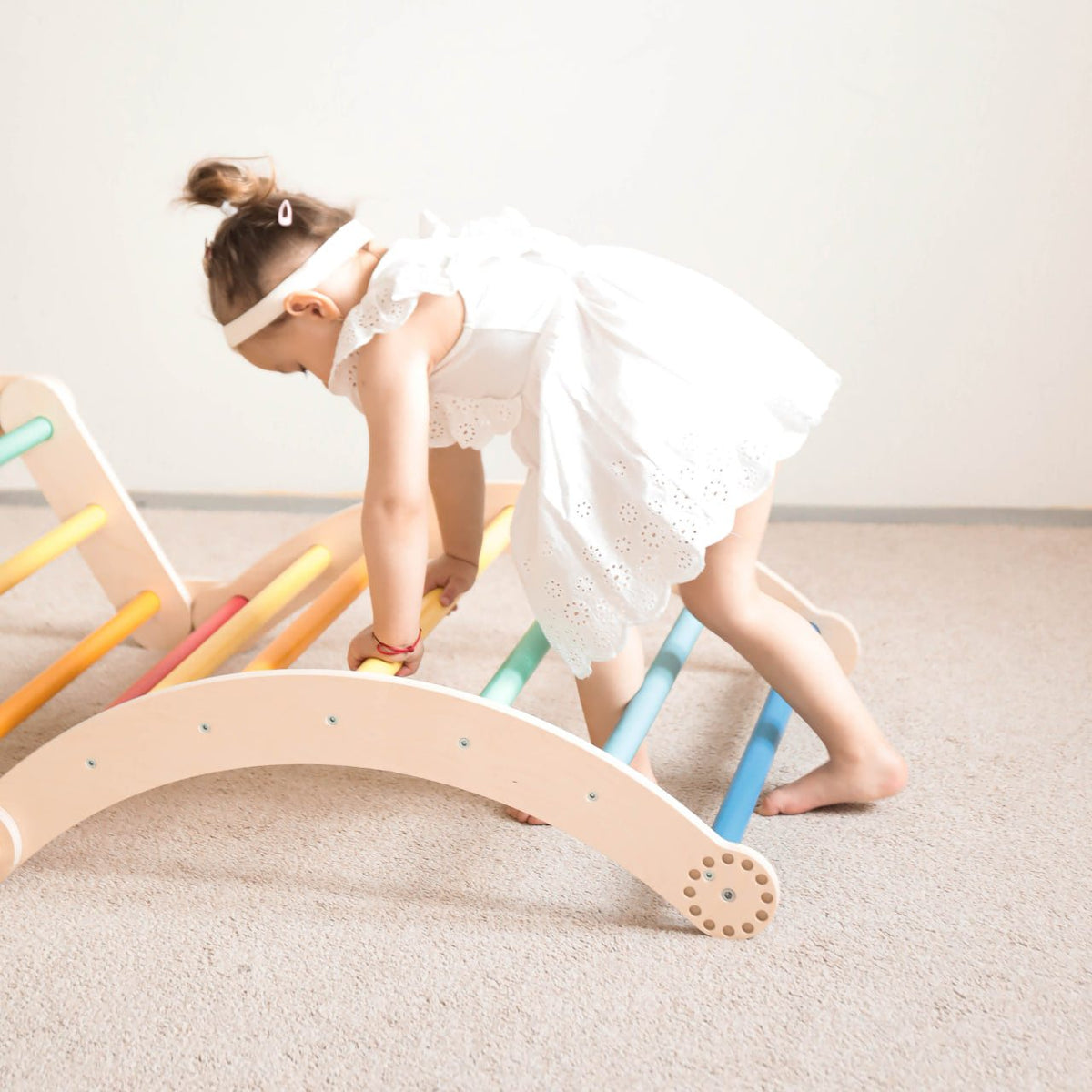 Child playing on a rainbow-colored wooden climbing frame set.