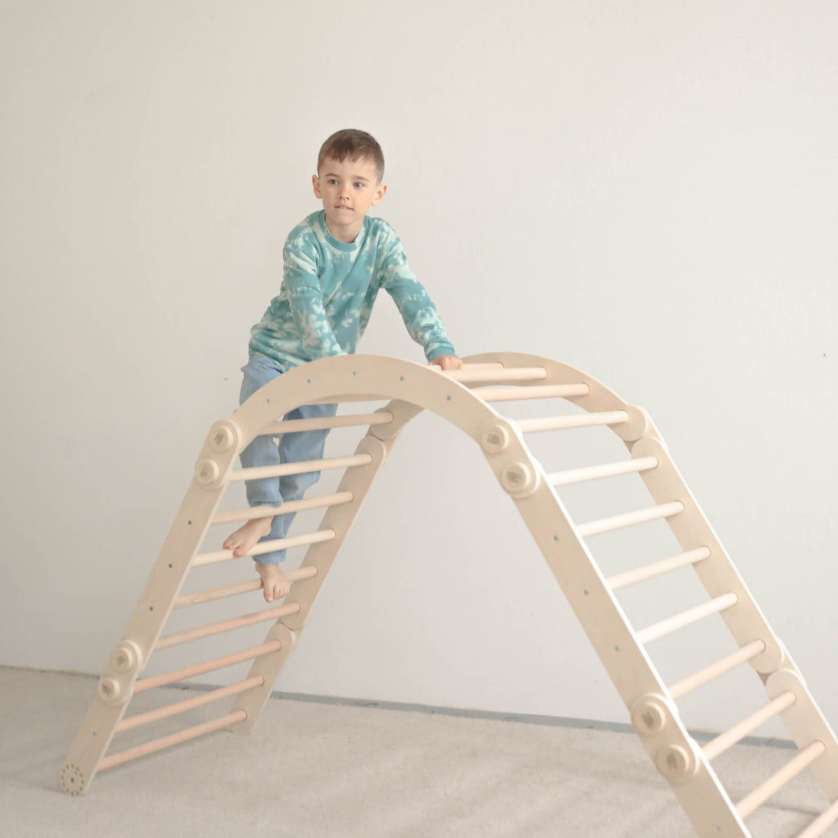 Child playing on natural wood climbing set indoors.