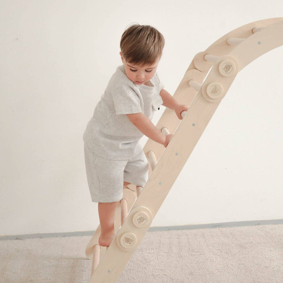 Child climbing natural wooden play set ladder indoors.