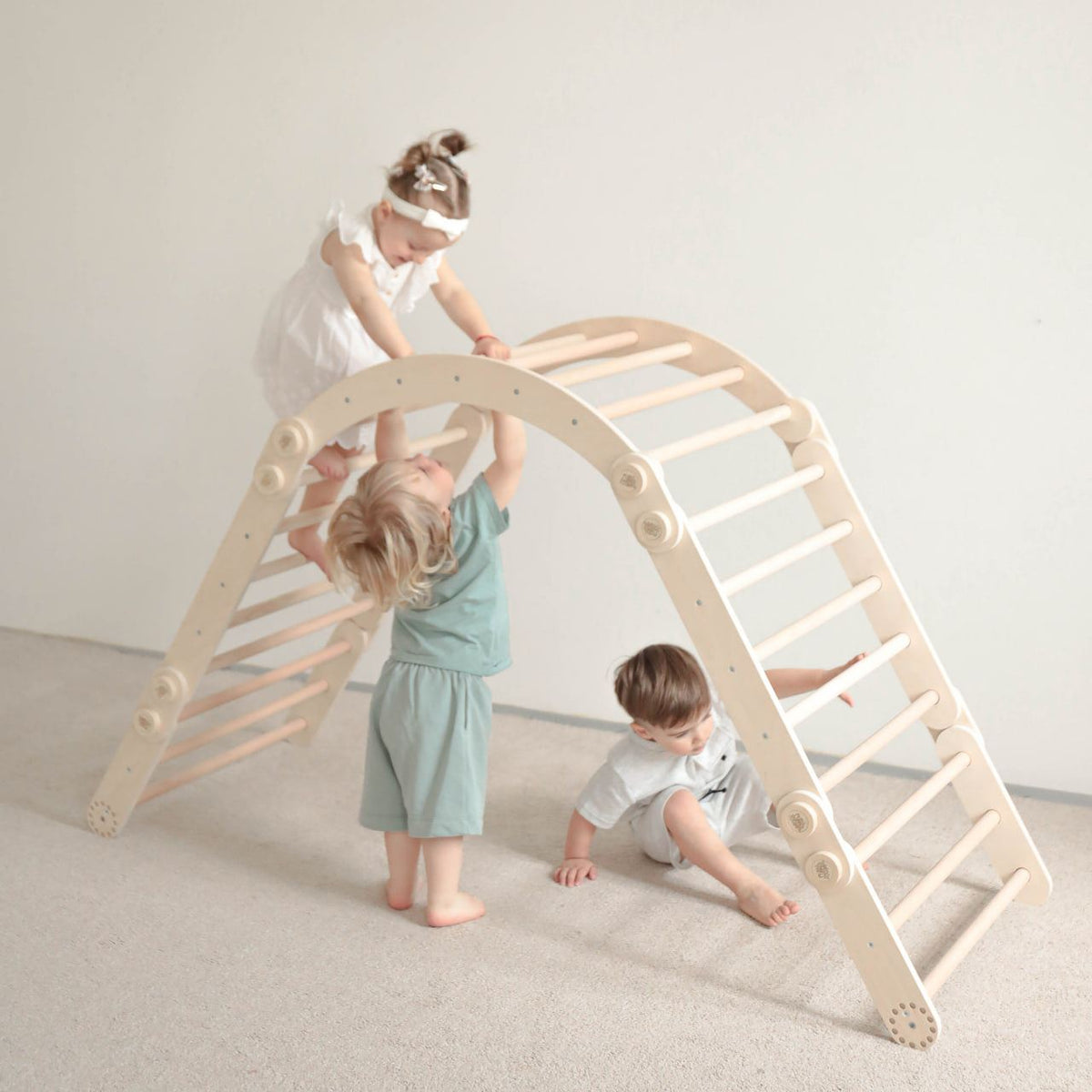 Children playing on natural wood climbing frame set indoors.