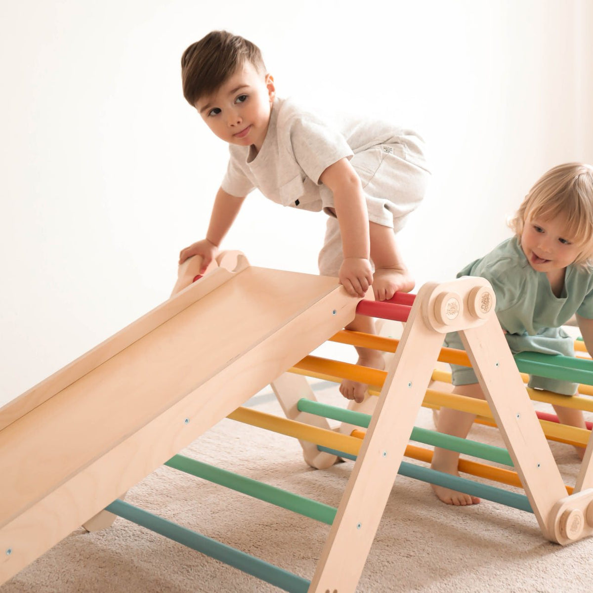 Children playing on a Flexi climbing frame with slide, featuring colorful Pikler triangles; perfect for indoor activity and motor skill development.