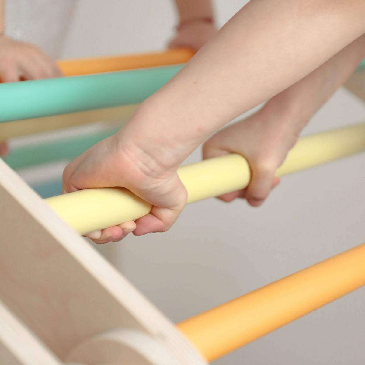 Child&#39;s hands gripping colorful bars of a flexi climbing set for kids, showcasing the product&#39;s durable birch wood construction.
