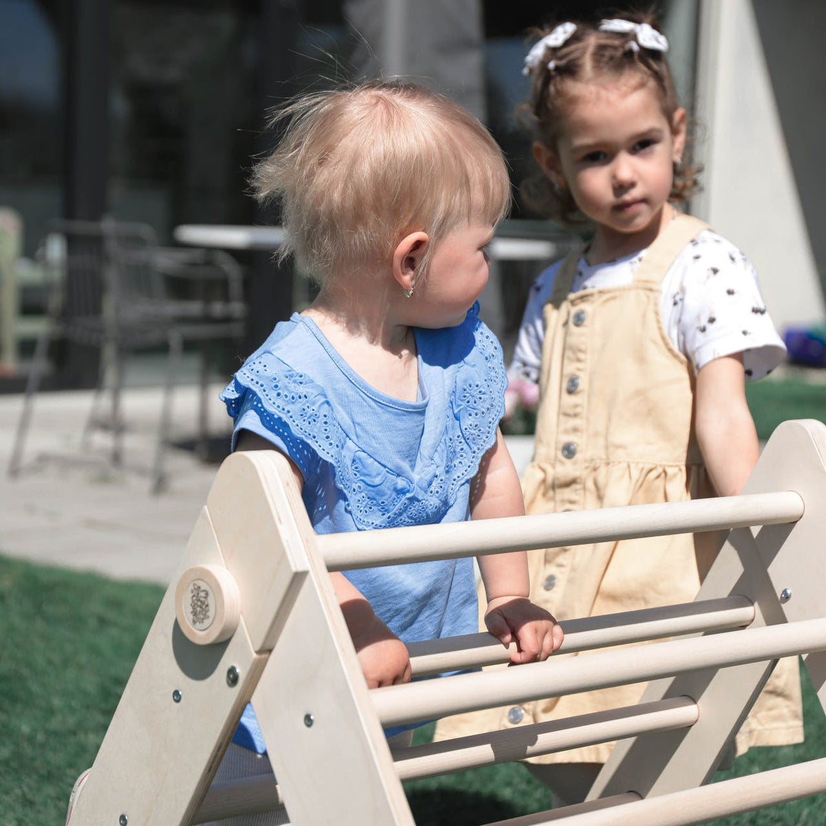 Children playing on a natural wooden Pikler triangle outdoors.