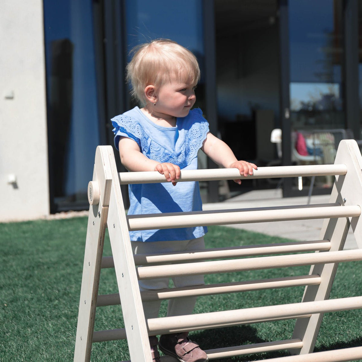 Toddler playing with a wooden Pikler climbing triangle outdoors, enhancing motor skills and balance.
