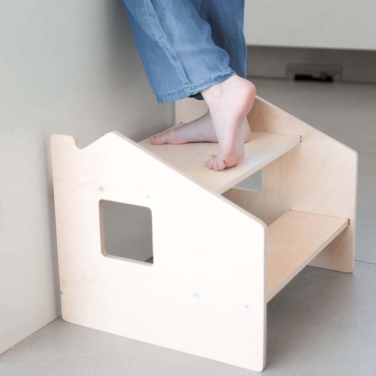Child using a Montessori-Tritthocker with two steps for easy reaching, made from durable birch plywood, ideal for fostering independence.