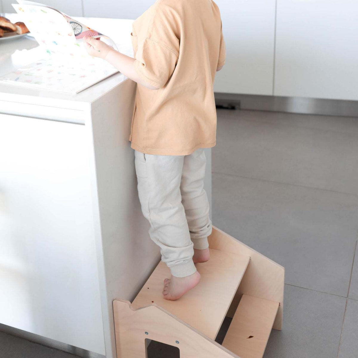 Child using Montessori-Tritthocker learning tower in kitchen.