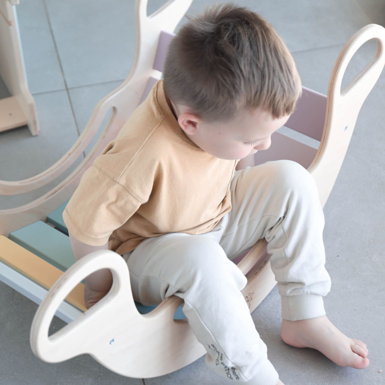 Child playing on a pastel-colored balance rocker made of birch plywood.