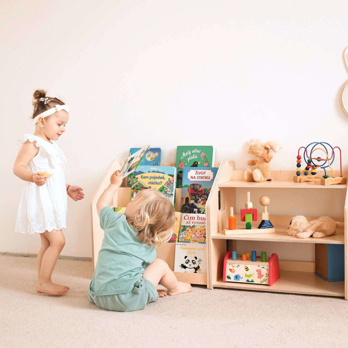 Montessori Bücherregal und Spielzeugregal im Kinderzimmer mit spielenden Kindern.