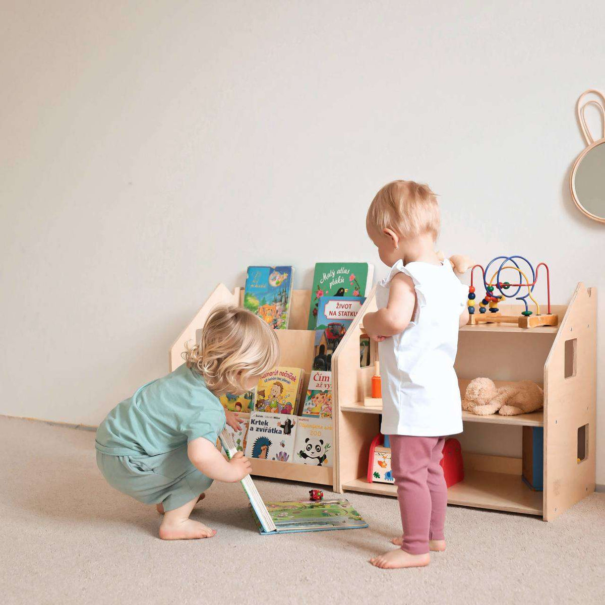 Children interacting with the Bücherregal &amp; Spielzeugregal, organized under Montessori principles, showcasing books and toys.
