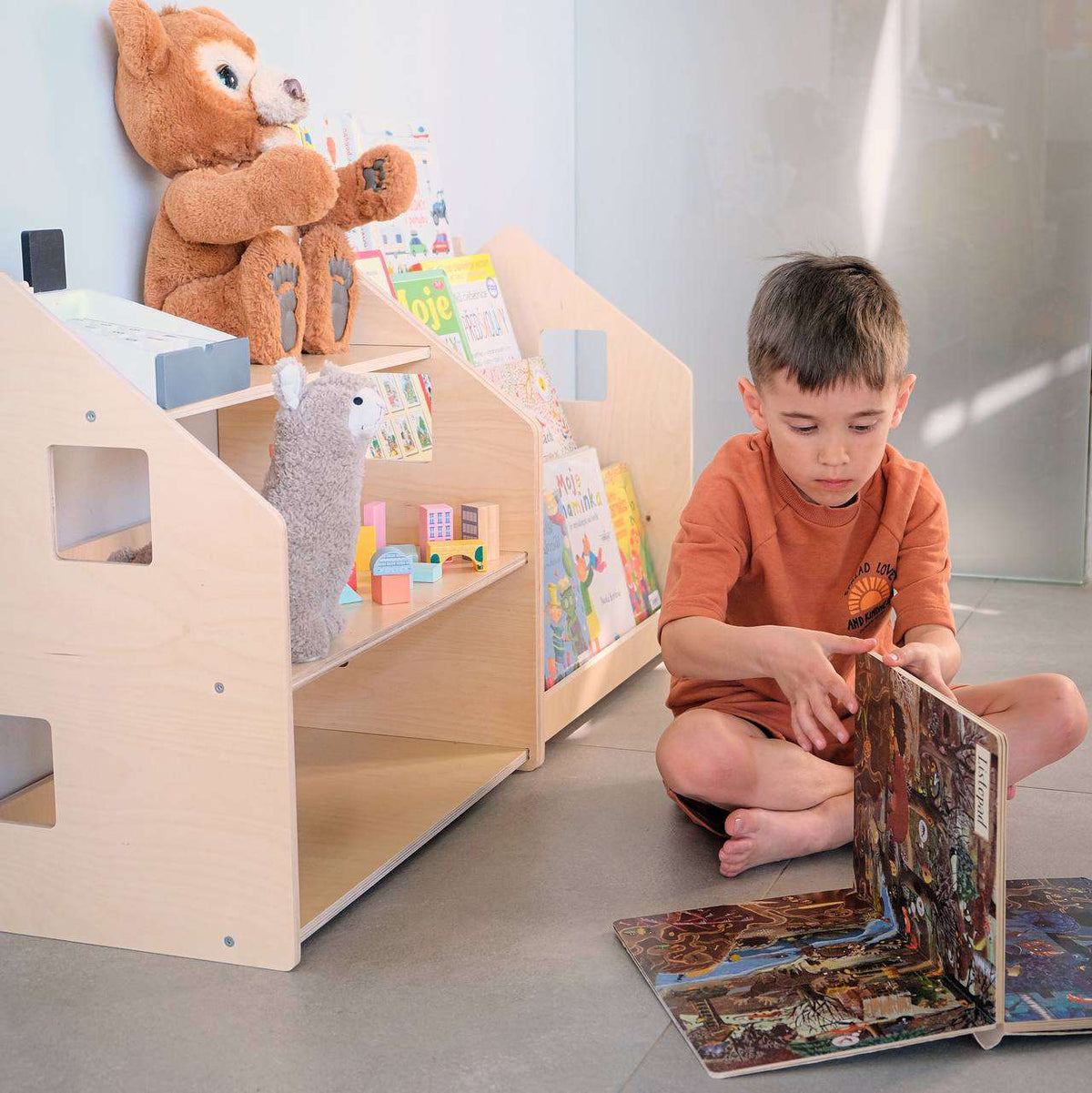 Child reading by Montessori-inspired bookshelf and toy shelf in a nursery.