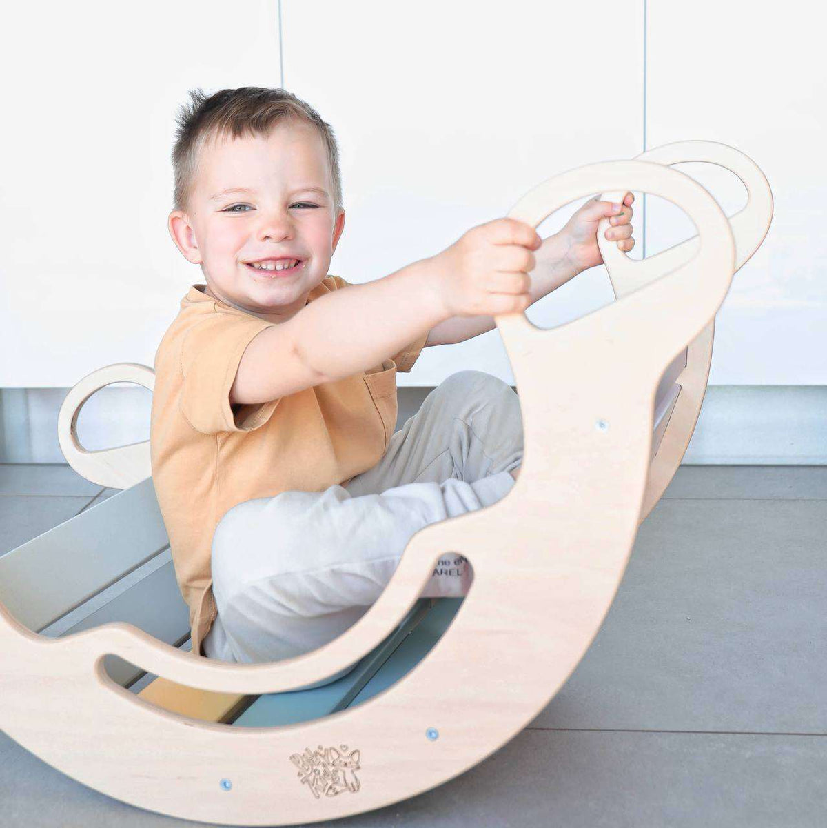 Child enjoying a pastel-colored wooden rocker, showcasing versatility for play and balance activities indoors.