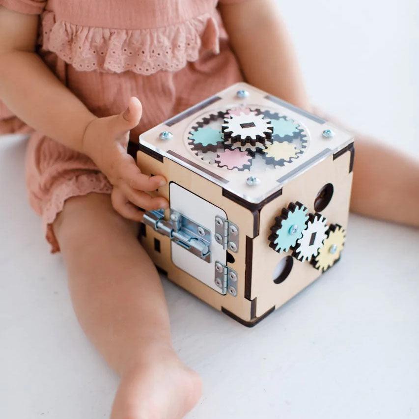 Interactive wooden learning cube for babies and toddlers, featuring gears and latches for fine motor skill development.
